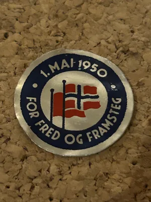 Rundt 1. mai-merke av tynt aluminium fra 1950, med fire røde faner og mørkeblå tekst «For fred og framsteg».