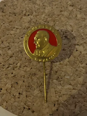 Rundt gullfarget 1. mai-merke fra 1957 med profilportrett av A. E. Gundersen mot rød bakgrunn.