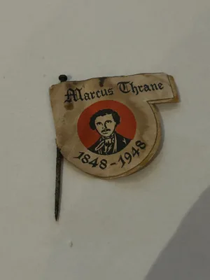 Papirmerke fra 1948 med portrett av Marcus Thrane foran rødt felt, festet med metallnål.